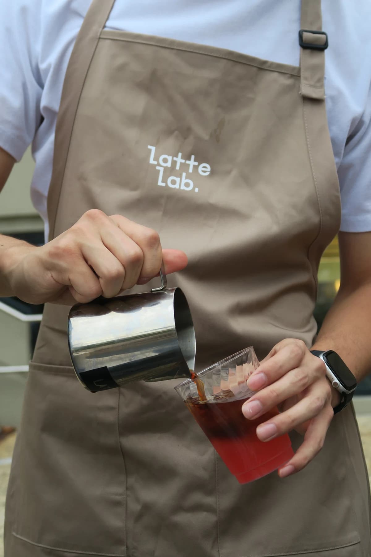 A person wearing a Latte Lab apron pouring coffee into a glass