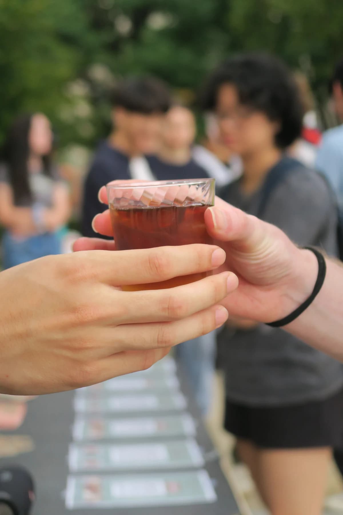 Hands passing a glass of coffee at an outdoor gathering